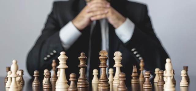 A person in a suit sitting behind a chessboard with their hands together in a "ready to play" position.